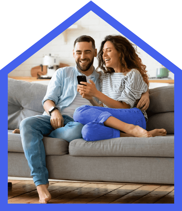 A young couple sitting on a couch enthusiastically viewing Rent.com property listings